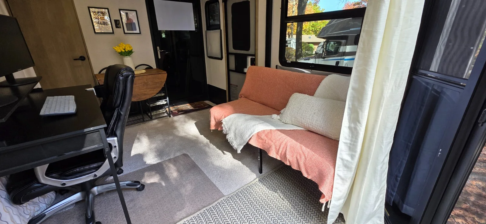 Toy-hauler studio arranged with a writing desk, lounge seating, and dining table